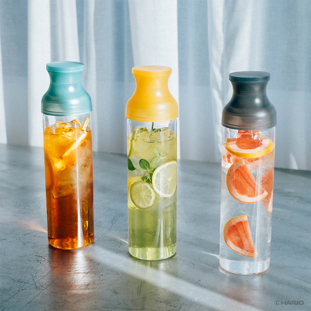 HARIO Filter-in Carafes with green, yellow and grey caps, filled with iced tea, lemon and grapefruit, standing in sunlight