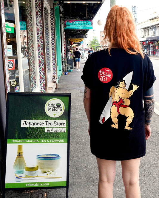 A black organic cotton t-shirt with a graphic print of a Japanese sumo wrestler holding a surfboard, with EdoMatcha logo.