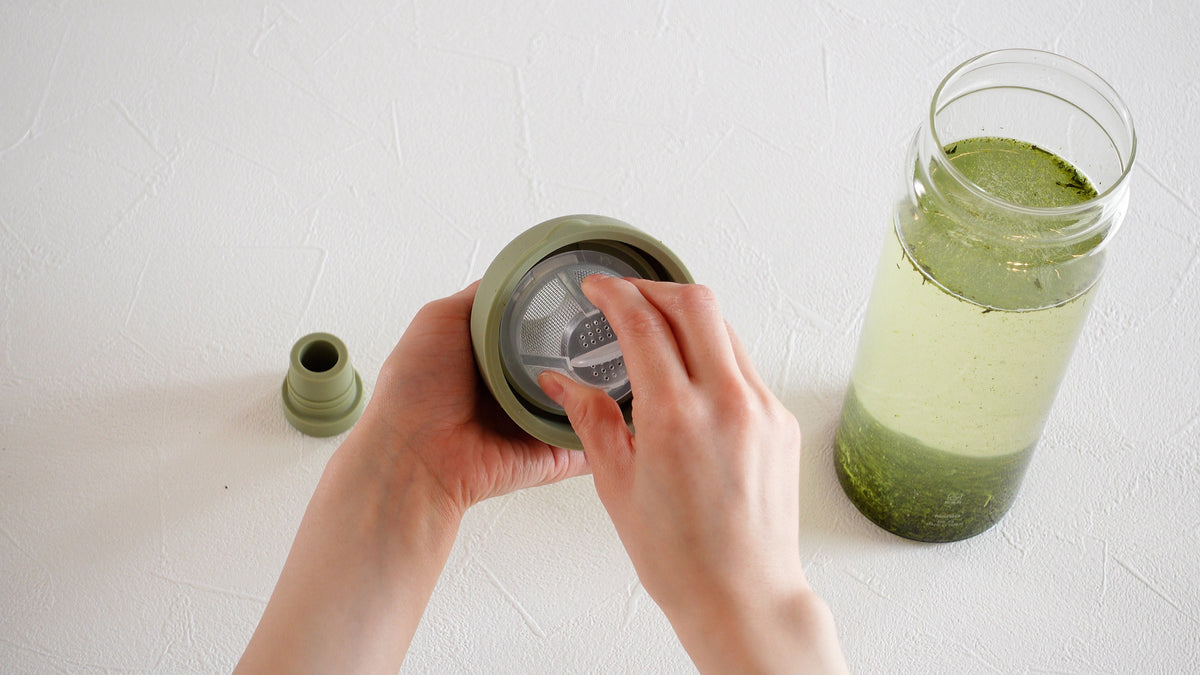 Fitting the mesh filter into the spout of a HARIO Filter-in Bottle 750ml smoky green, with the bottle of cold brew beside it