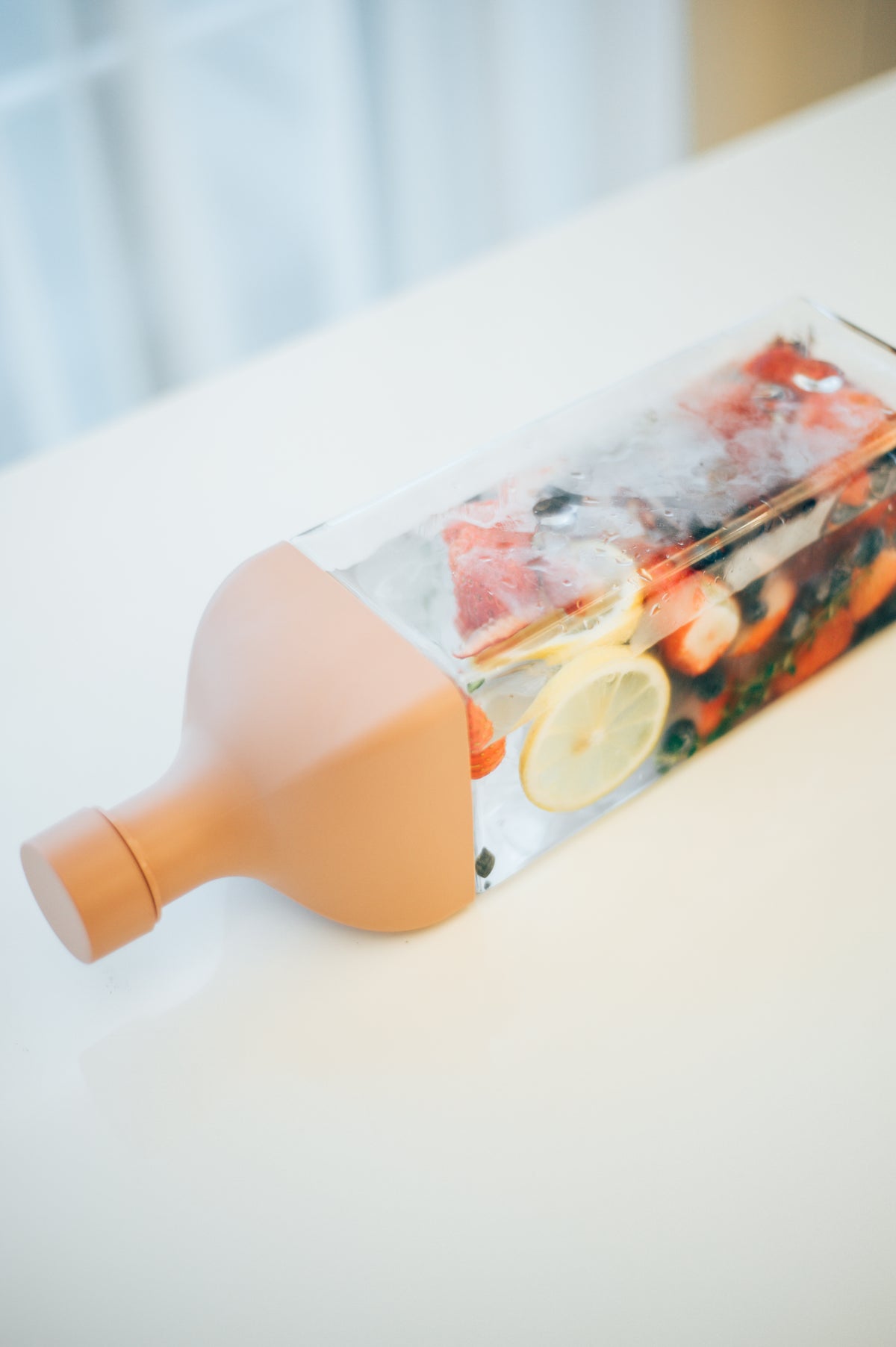 HARIO Ka-Ku Bottle 1,200ml smoky pink lying on a white table, filled with strawberries, lemon and blueberries