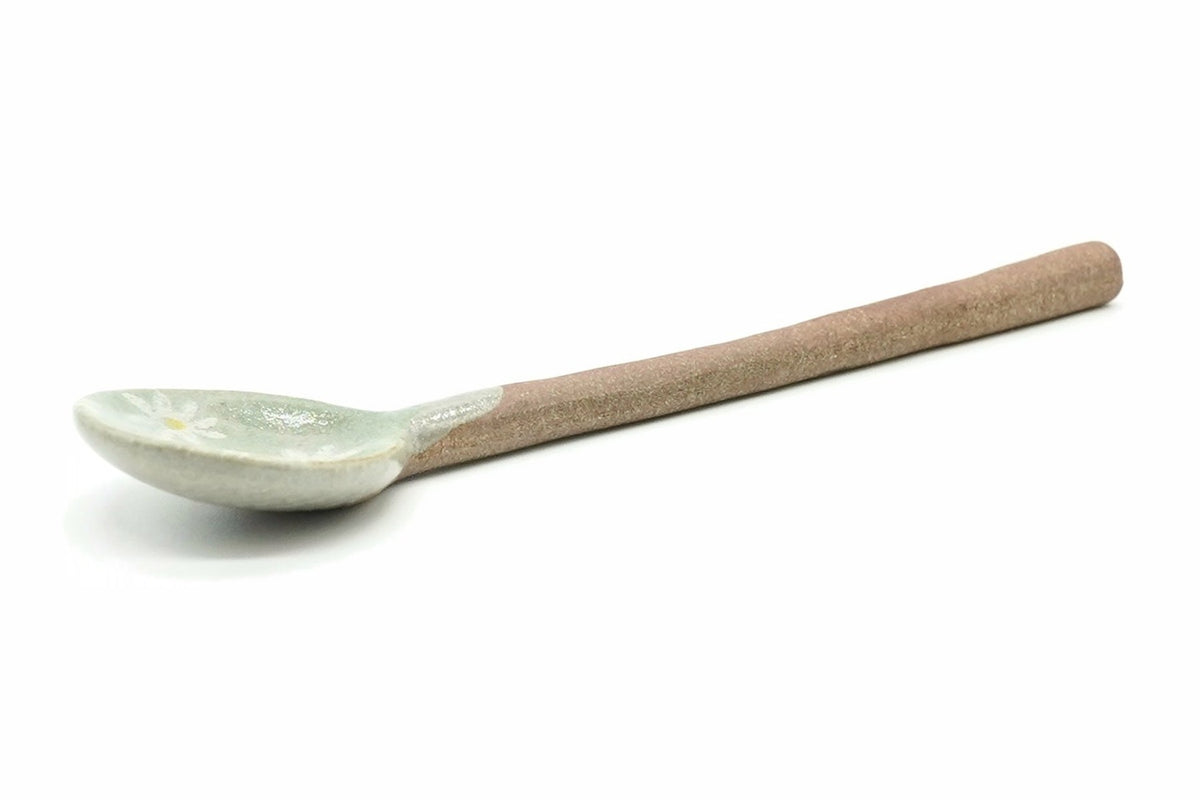 Nobana Ceramic Tea Spoon, a small spoon with a pale green bowl, a white daisy-like flower and a long reddish-brown clay handle, seen from the side