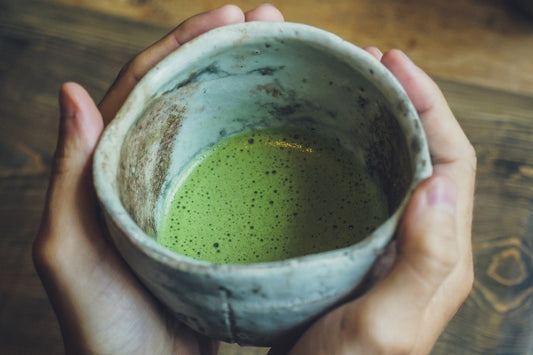 Hands cradling a Japanese chawan of freshly whisked matcha with a fine green foam