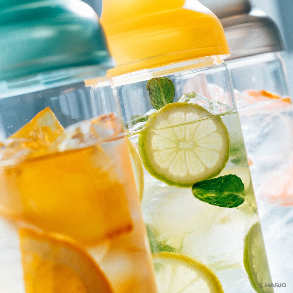 Three HARIO Filter-in Carafes with green, yellow and grey caps filled with iced tea, citrus and grapefruit