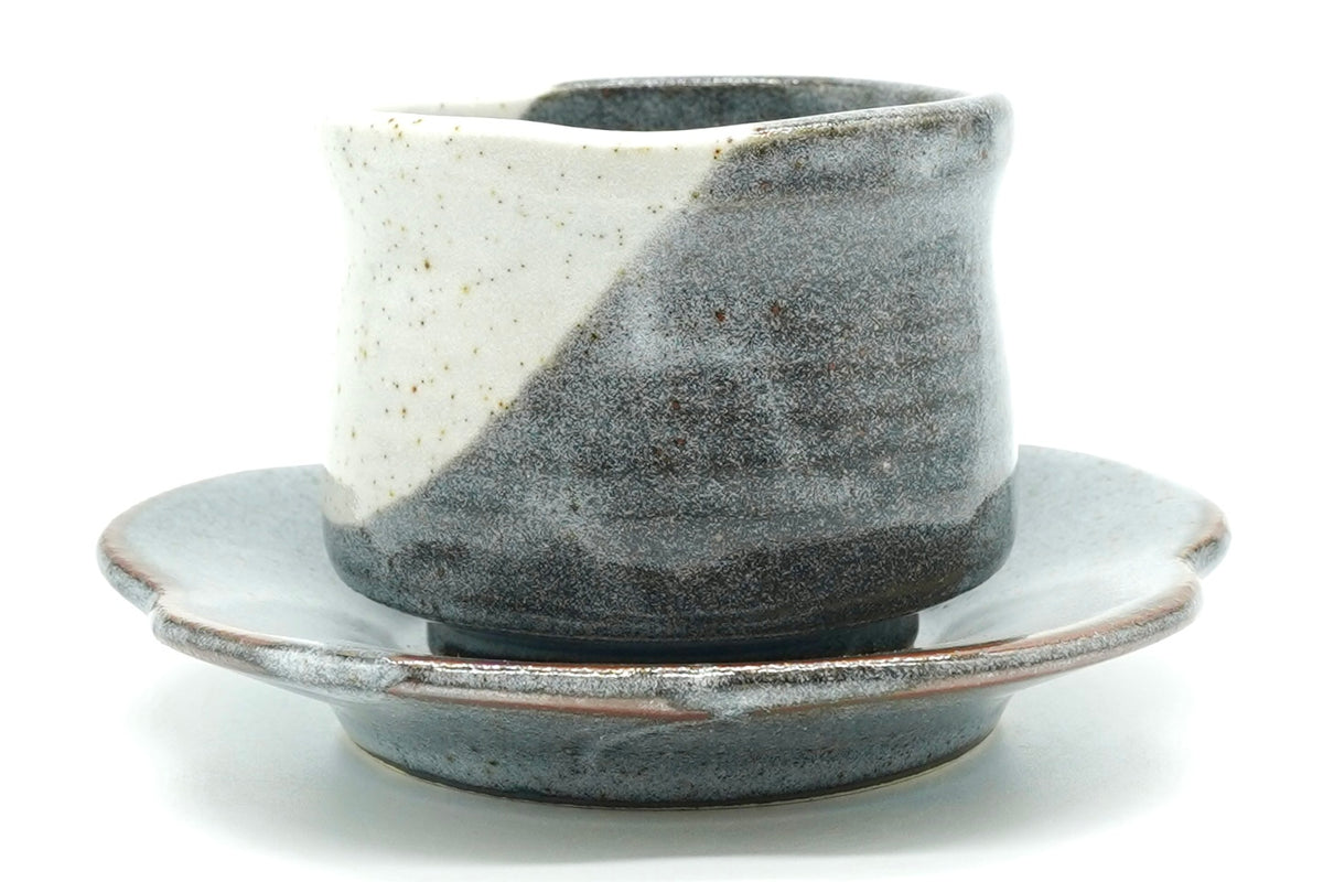 Tsukikage Yunomi cup on its flower-shaped saucer, speckled white and slate blue-grey glazes meeting in a diagonal