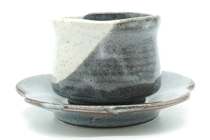Tsukikage Yunomi cup on its flower-shaped saucer, speckled white and slate blue-grey glazes meeting in a diagonal