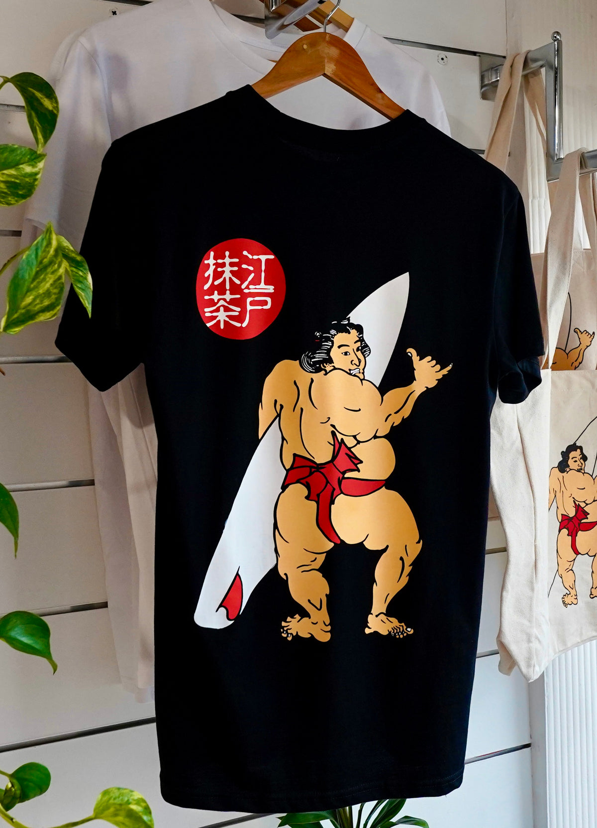 A black organic cotton t-shirt with a graphic print of a Japanese sumo wrestler holding a surfboard, with EdoMatcha logo.
