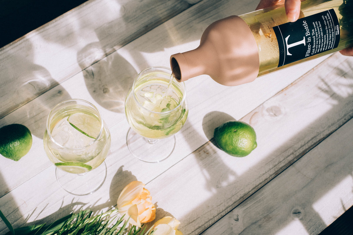 Pouring cold-brewed tea from a HARIO Filter-in Bottle 750ml smoky pink into glasses with lime on a sunny table