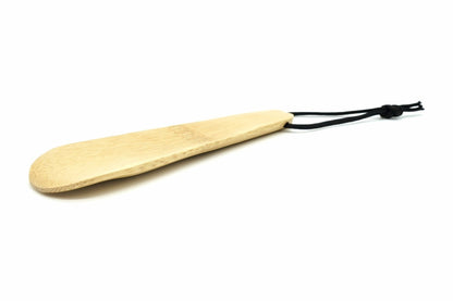 Bamboo Cha-saji, a flat bamboo scoop with a rounded blade and a black cord loop at the handle end, seen from a low angle