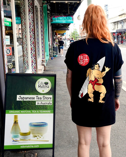 A black organic cotton t-shirt with a graphic print of a Japanese sumo wrestler holding a surfboard, with EdoMatcha logo.