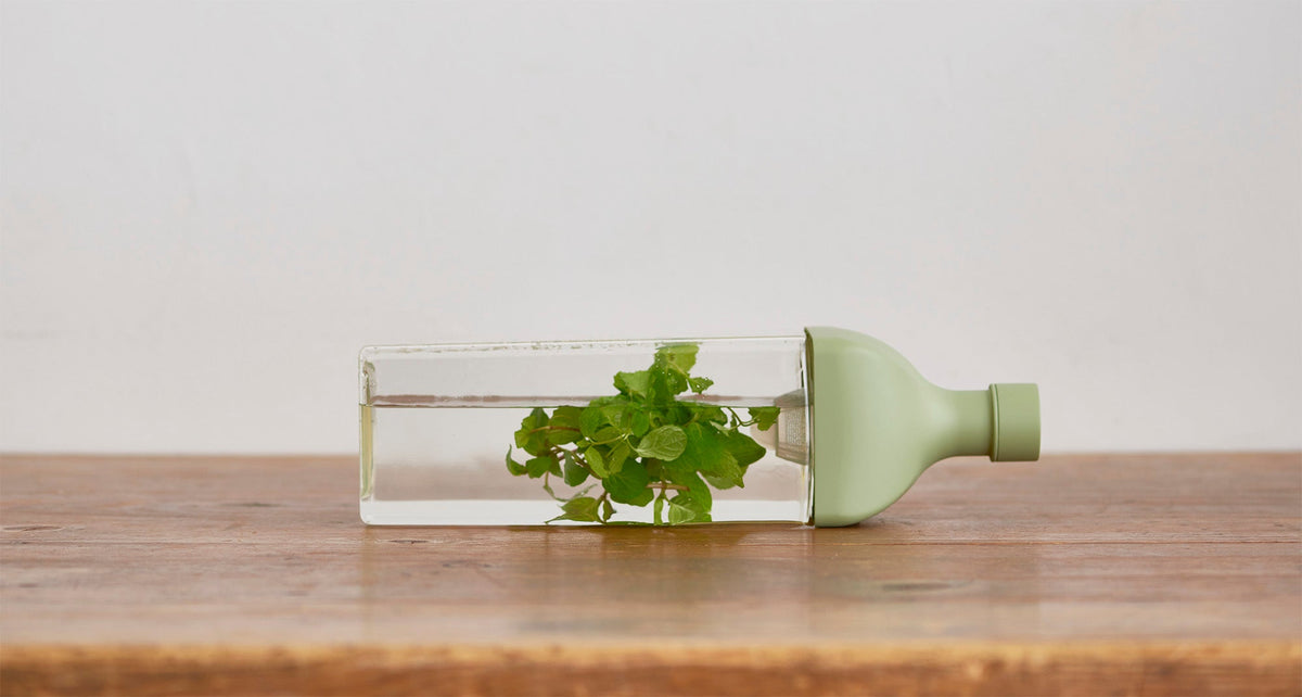 HARIO Ka-Ku Bottle 1,200ml smoky green lying on its side on a wooden table, filled with water and fresh mint