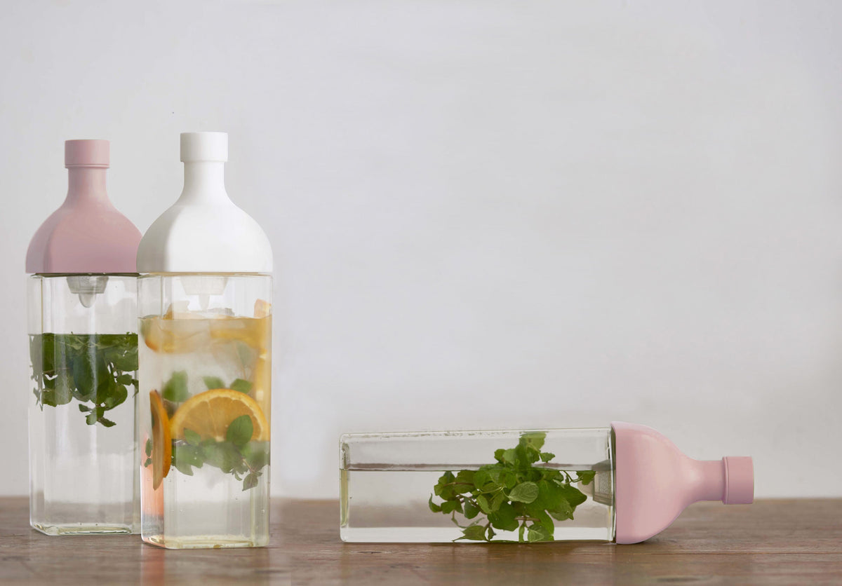 HARIO Ka-Ku Bottles in smoky pink, white and smoky green on a wooden table, filled with mint, orange and cold brew