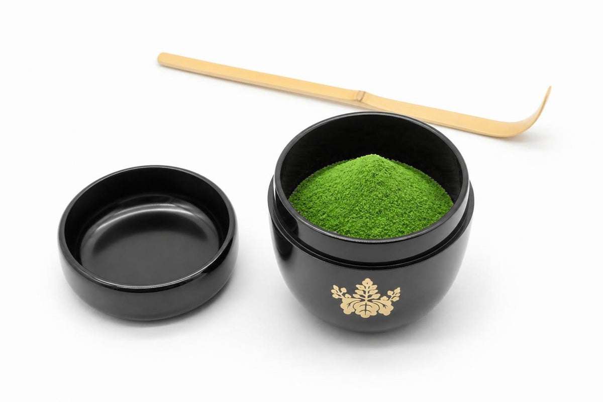 Kikumon Natsume in black, open, with matcha heaped inside, its lid set beside it with the inside facing up, and a bamboo chashaku behind