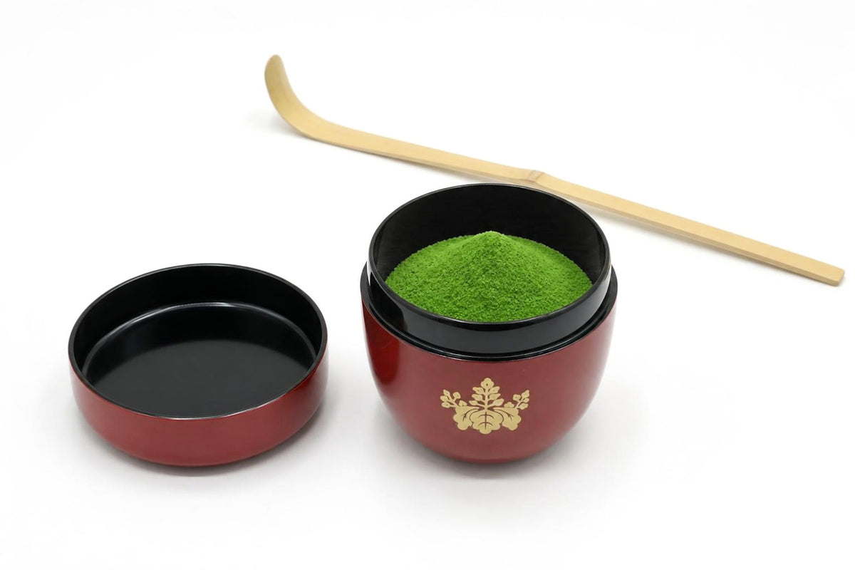 Kikumon Natsume in red, open, with matcha heaped inside, its lid set beside it with the inside facing up, and a bamboo chashaku behind