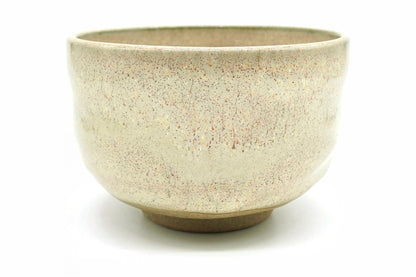 Kinari Yunomi, a bowl-shaped teacup in a pale cream glaze flecked with fine rust-red specks, with a bare brown foot
