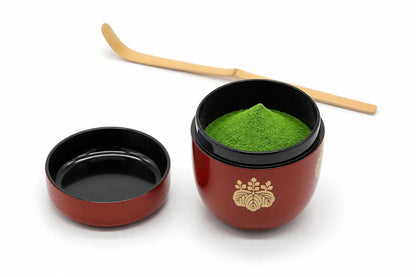 Kōdaiji Natsume in red, open, with matcha heaped inside, its lid set beside it with the inside facing up, and a bamboo chashaku behind