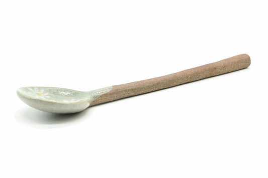 Nobana Ceramic Tea Spoon, a small spoon with a pale green bowl, a white daisy-like flower and a long reddish-brown clay handle, seen from the side