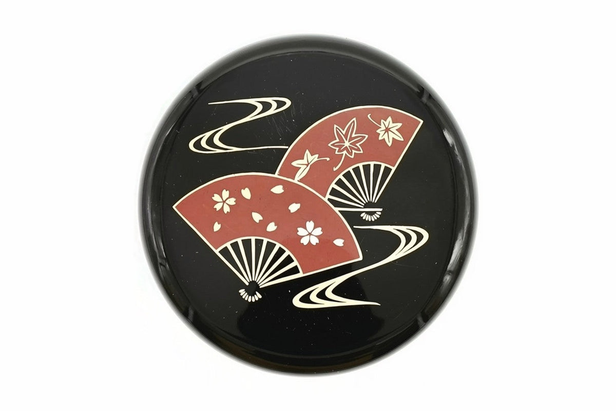 Lid of the black Ōgi Natsume from above, two red folding fans, one with cherry blossoms and one with maple leaves, over gold flowing water