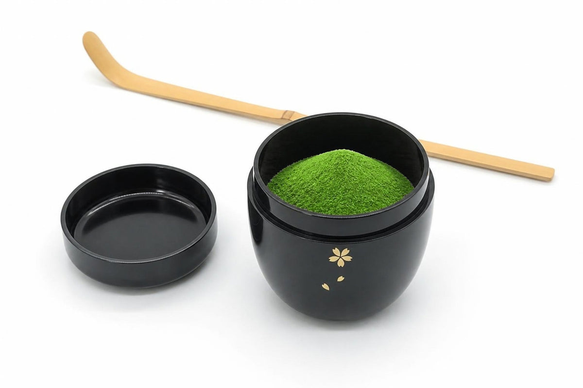 Ōgi Natsume in black, open, with matcha heaped inside, its lid set beside it with the inside facing up, and a bamboo chashaku behind