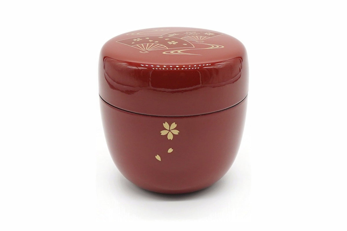 Ōgi Natsume in red, a glossy matcha caddy with a gold cherry blossom and falling petals on the body and folding fans on the lid