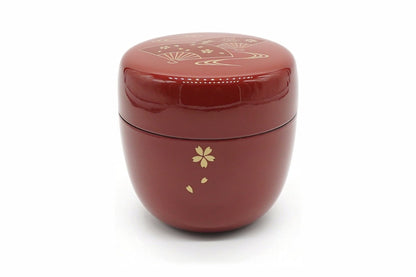 Ōgi Natsume in red, a glossy matcha caddy with a gold cherry blossom and falling petals on the body and folding fans on the lid