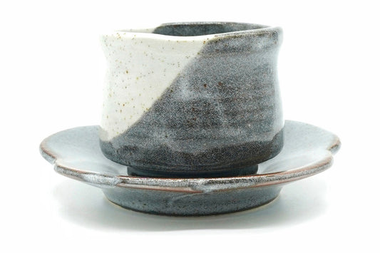 Tsukikage Yunomi cup on its flower-shaped saucer, speckled white and slate blue-grey glazes meeting in a diagonal