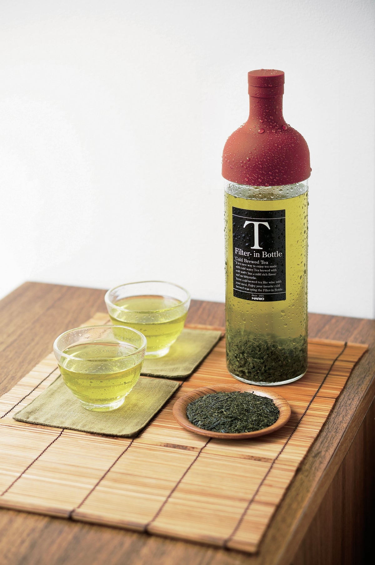 HARIO Filter-in Bottle 750ml red on a bamboo mat with two glasses of cold-brewed sencha and a dish of tea leaves